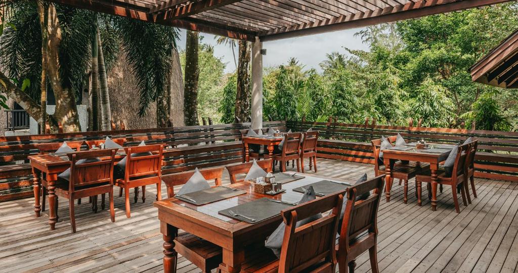 Kafejnīca ar koka galdiem un krēsliem, izvietota brīvā dabā, ieskauta zaļajā ainavā. Daba un relaksējoša atmosfēra rada patīkamu ēdināšanas pieredzi.