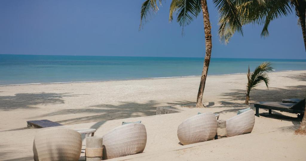 Pludmales ainava ar sēdvietām un palmām, skaidra debesis un mierīgs jūras skats. Ideāla vieta relaksācijai un atpūtai.