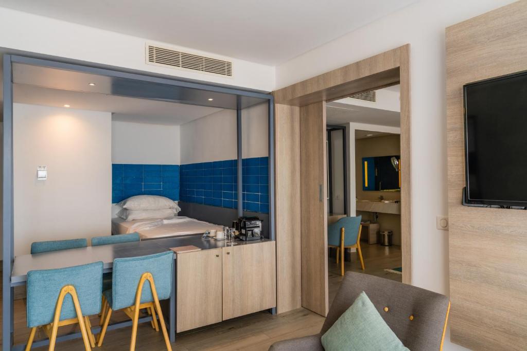 Mūsdienīgs viesnīcas numurs ar zilu flīžu sienu, ērtu gultu un viesistabu, kas aprīkota ar galdu un krēsliem. Numurā ir televizors un piekļuve vannas istabai.