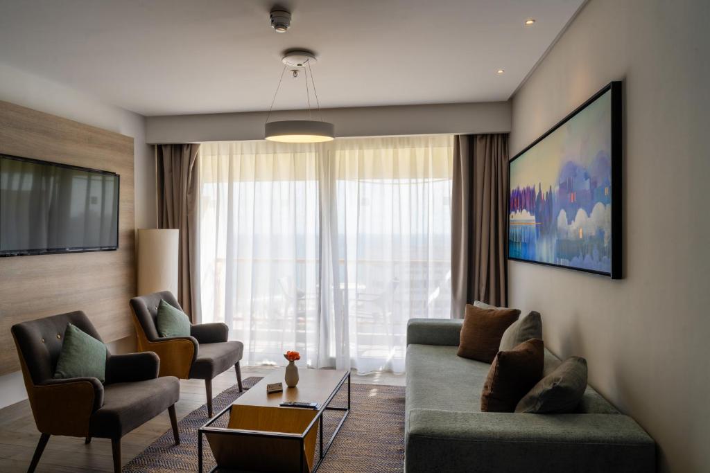 Mūsdienīgs viesnīcas numurs ar plašu dzīvojamo telpu, kurā ir dīvāns, krēsli un televizors. Lielie logi nodrošina daudz dabiskā apgaismojuma un skatu uz ārpusi.