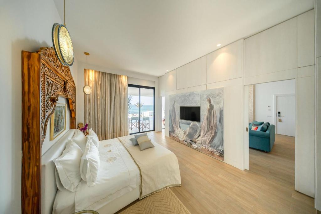 Mūsdienīgs guļamistabas interjers ar greznu gultu, dabīgu apgaismojumu un lieliem logiem, kas paver skatu uz jūru. Telpā ir arī modernā televizora siena un ērta atpūtas zona.