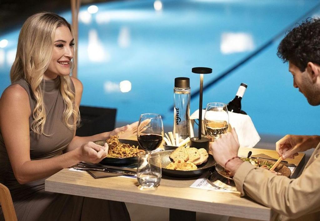 Elegantā romantiskā vakariņu aina pie galda ar dažādiem ēdieniem un dzērieniem, fonā redzams peldbaseins.