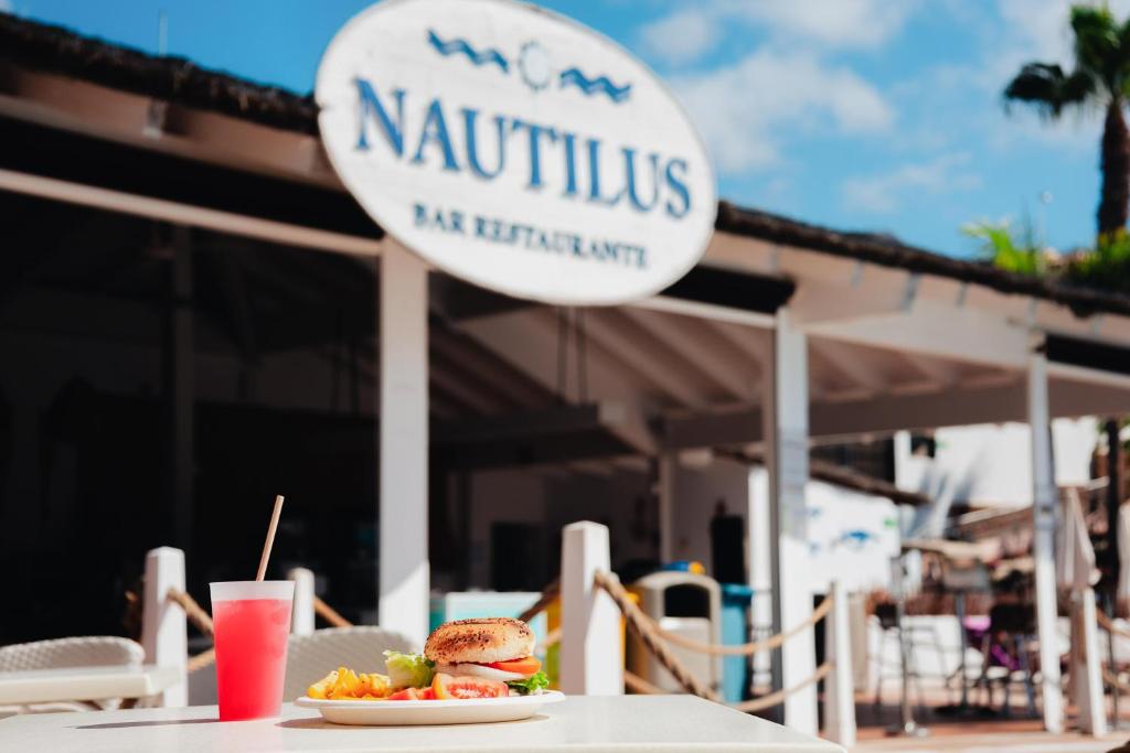 Restorāna "Nautilus" zīme fona un garšīgs burgeris ar frī kartupeļiem un dzērienu priekšplānā. Ideāla vieta relaksācijai un gardām maltītēm.