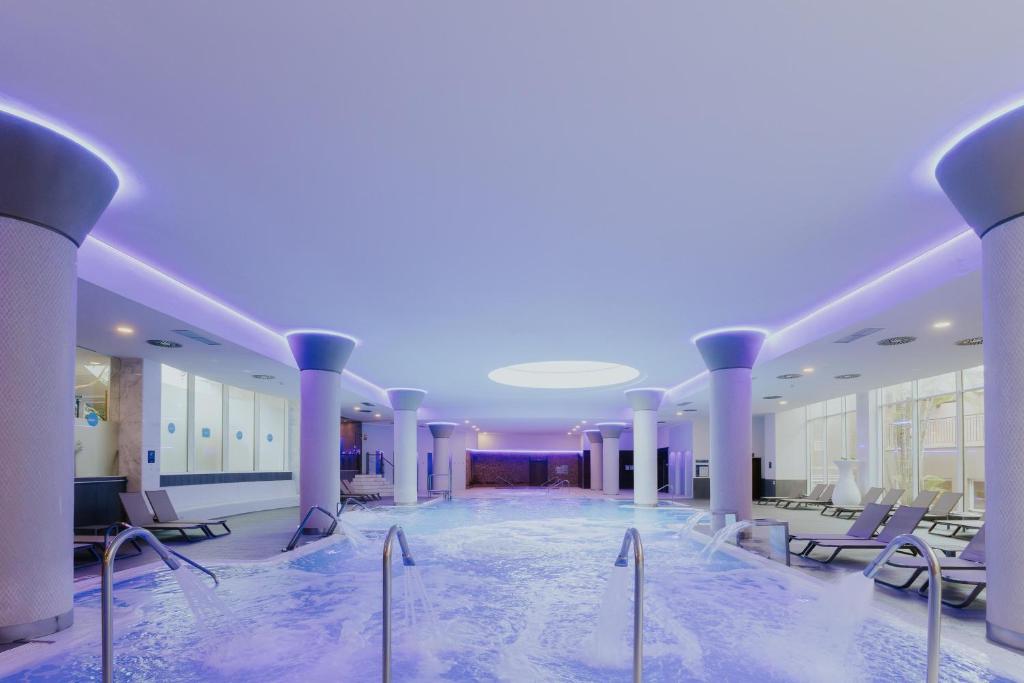 Mūsdienīgs spa ar relaksējošu ūdens baseinu un mīkstu apgaismojumu, kas rada mierīgu atmosfēru. Atpūtas krēsli un lieli logi nodrošina gaismas plūsmu un skatu uz ārpusi.