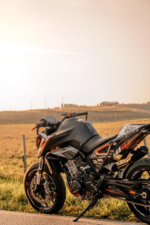 Sportiska motocikla attēls, kas novietots uz ceļa blakus zaļai pļavai, ar saulrieta gaismu, kas apgaismo ainu.