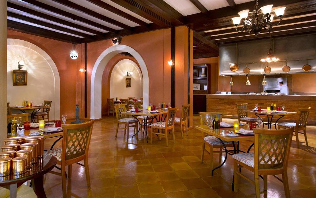 Elegants restorāns ar siltu apgaismojumu, koka griestiem un mājīgām galdiņām. Interjers raksturo arku formas un izsmalcinātu dekoru, radot patīkamu atmosfēru.