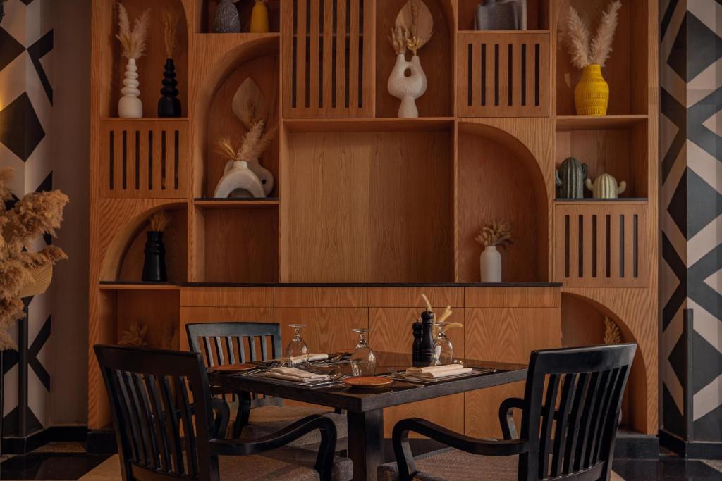 Mūsdienīga restorāna interjers ar elegantu koka plauktu, kas dekorēts ar mākslinieciskām vazo un augu kompozīcijām, un elegantu galdu ar galda piederumiem.