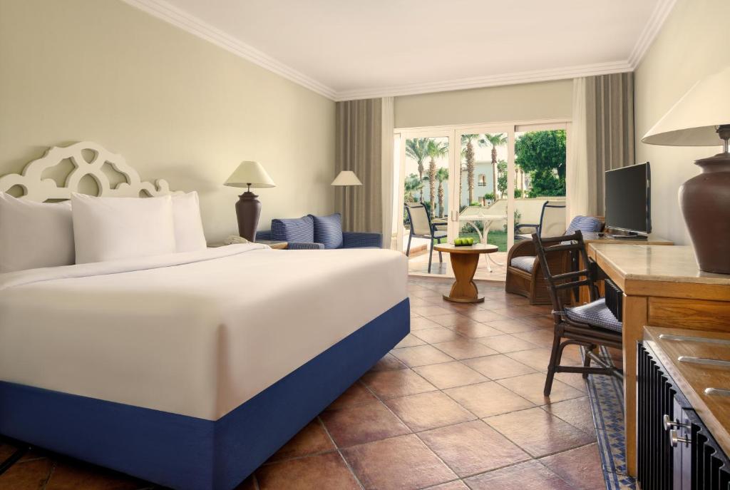 Moderns viesnīcas numurs ar lielu gultu, ērtu atpūtas zonu un skatu uz dārzu. Telpa ir gaiša un stilīga, ar koka mēbelēm un televizoru.