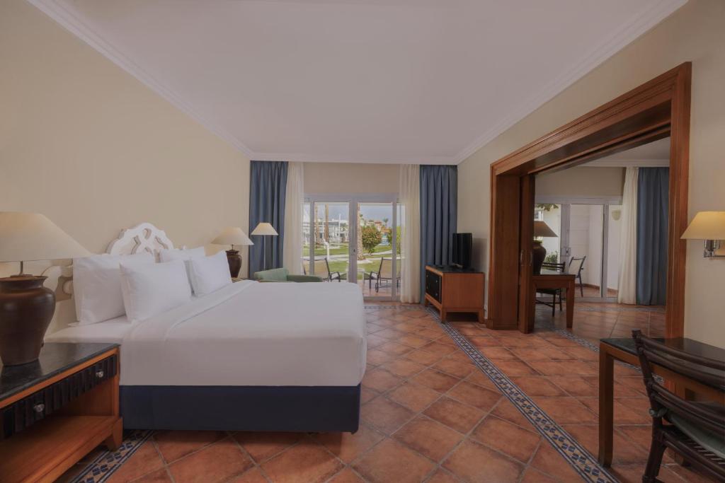 Mūsdienīga viesnīcas istaba ar plašu gultu, ērtām mēbelēm un skatu uz dārzu. Istabā ir televizors un dabiska gaisma, kas ieplūst caur logiem.