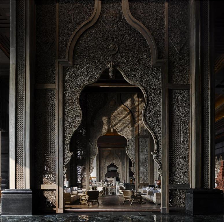 Elegants interjers ar arābu arhitektūras elementiem, kas attēlo plašu telpu ar greznu apdari un mūsdienīgu dizainu. Gaisma plūst caur dekoratīvajām durvīm, radot siltu atmosfēru.