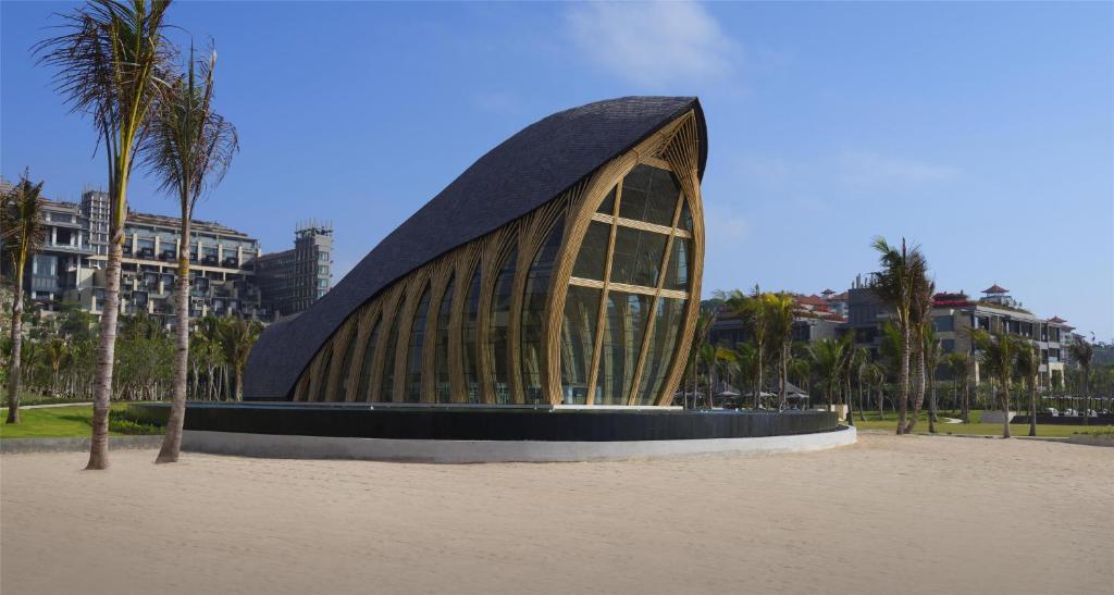 Mūsdienīga arhitektūra ar unikālu formu, kas izceļas pludmales ainavā, ieskauta palmām un zaļām terasēm.