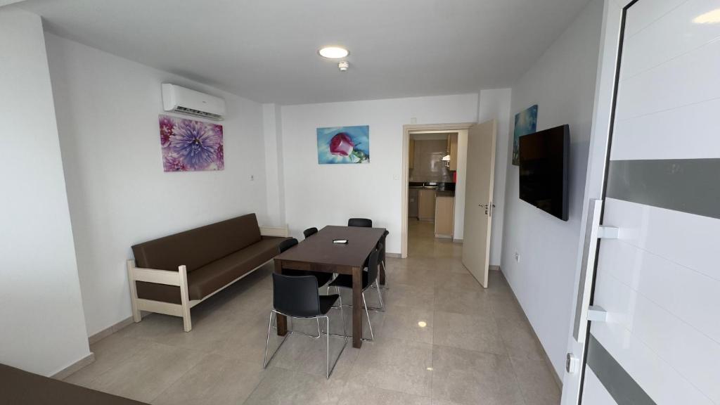 Gaiša un moderni iekārtota viesistaba ar brūnu dīvānu, galdu un melnām krēsliem, uz sienām ir krāsaini mākslas darbi.