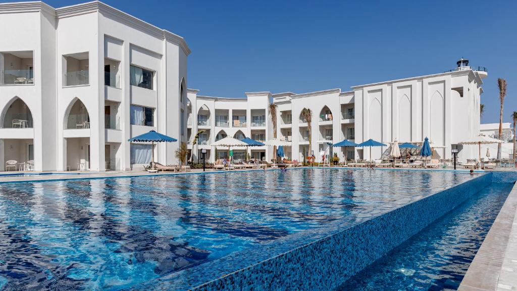 Sunrise Remal Beach Resort baseins ar baltām ēkām un saules gultām piekrastē.