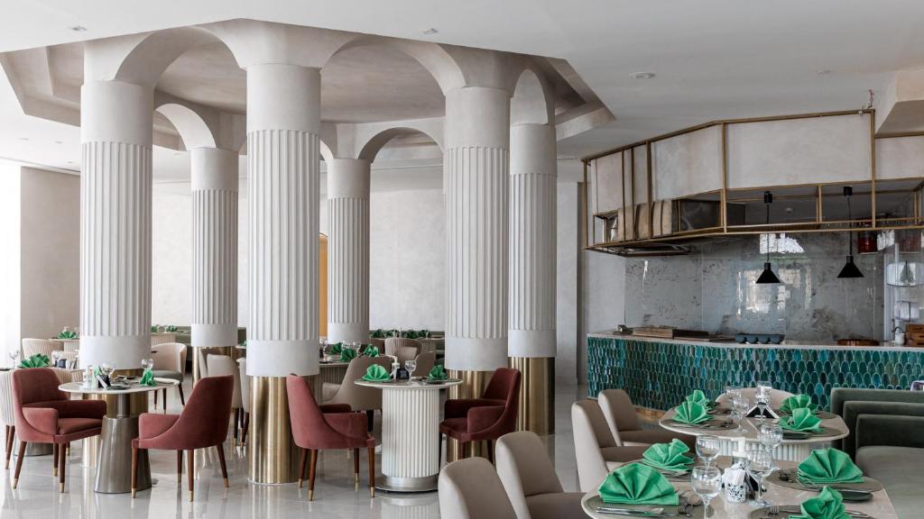 Elegants restorāns Sunrise Remal Beach Resort ar stilīgām kolonnām un zaļiem galda piederumiem.