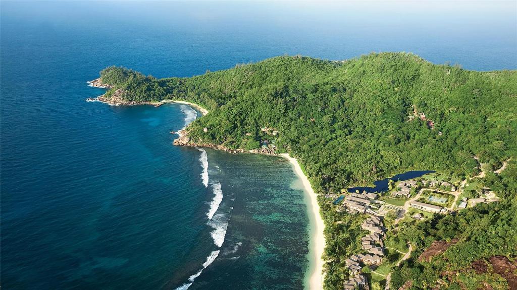 Kempinski Seychelles Resort skats no gaisa uz tropu piekrasti, pludmali un zaļajiem kalniem.