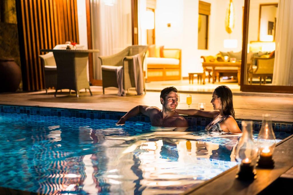 Romantisks brīdis pāris, kas atpūšas pie baseina, apgaismots ar siltām gaismām un relaksējošu atmosfēru.