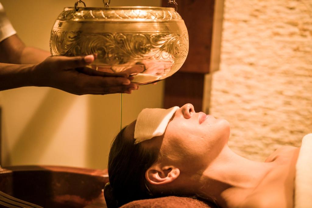 Atslābjoša masāža ar eļļu, kur sievietei uz acīm ir plānas drāniņas, bet virs viņas galvas tiek turēts rotāts trauks ar eļļu.