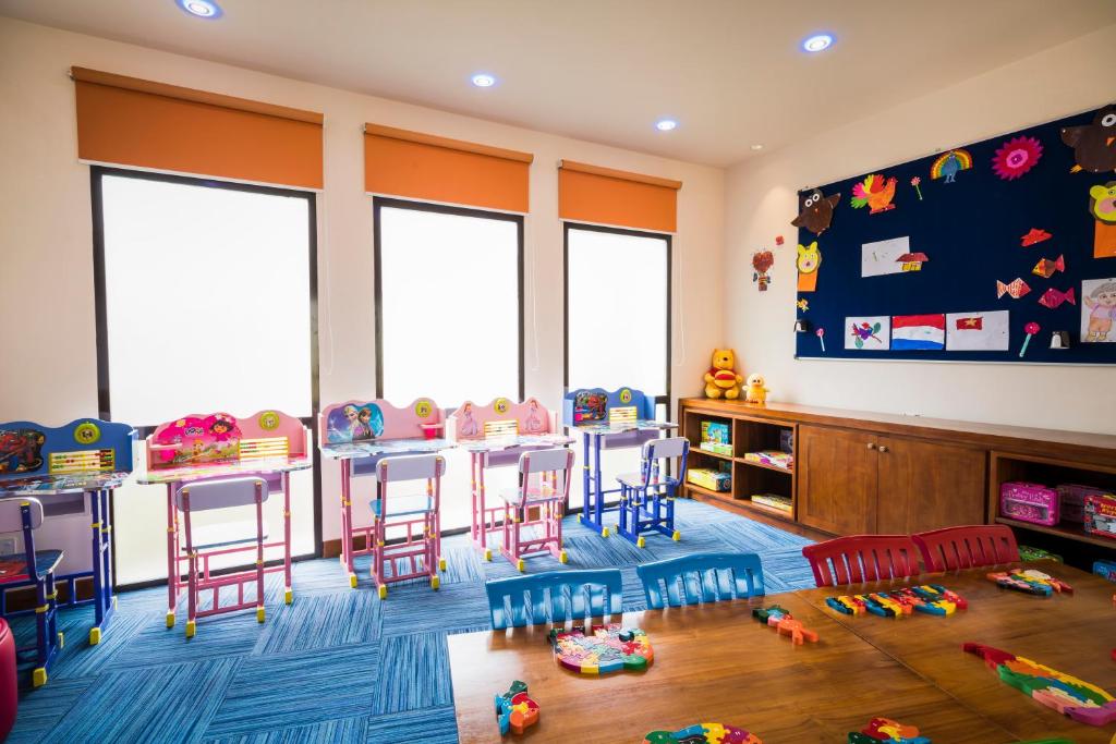 Krāsaina bērnu mācību telpa ar galdiem un krēsliem, kas rotāti ar rotaļlietām un mākslas darbiem uz sienas. Telpā ir daudz dabiskās gaismas, un tā ir iekārtota draudzīgā un radošā atmosfērā.