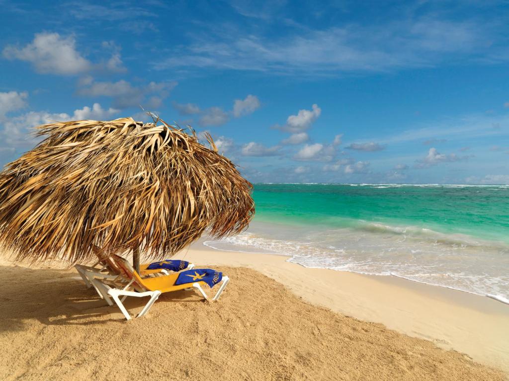 Pludmales sēžamkrēsls ar salmu nojumi, blakus skaistai jūrai un smilšu krastam. Būtiska pludmales atmosfēra ar zilu debesi un viļņiem.