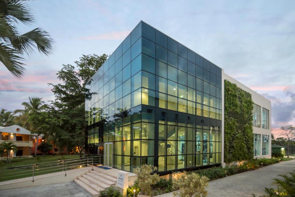 Mūsdienīgs stikla ēku dizains ar zaļo augu fasādi, apņemta ar ainavu un zilo debesu fonu. Ideāls piemērs mūsdienu arhitektūrai.