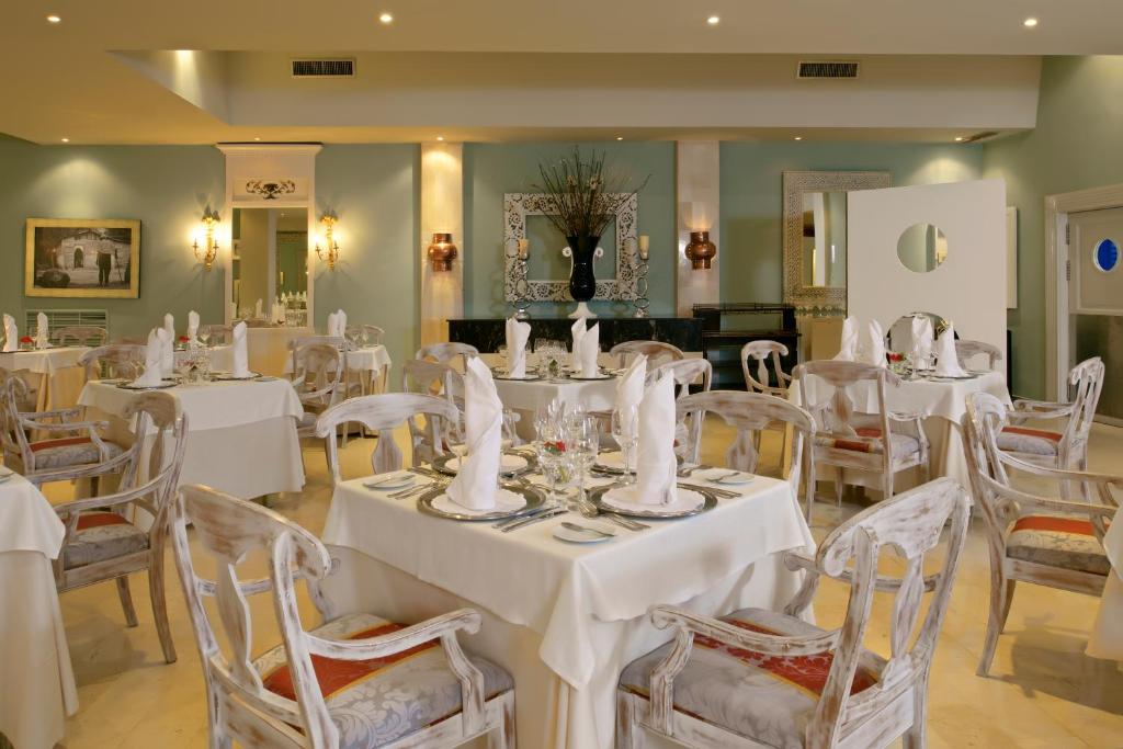 Elegants restorāna interjers ar baltām galdautām un dekoratīvām krēsliem, kas radīts patīkamai ēdināšanas atmosfērai. Gaisma un krāsu saskaņa piešķir telpai mierīgu un izsmalcinātu raksturu.