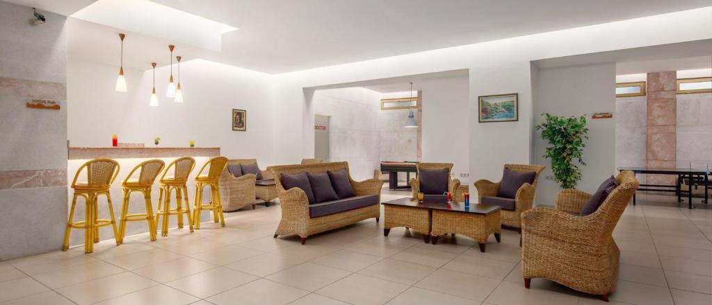 Mūsdienīgs viesnīcas interjers ar viesistabu, kas iekārtota ar rattan mēbelēm, elegantām lampām un bāra zonu. Gaismas tonis un augu klātbūtne rada mājīgu atmosfēru.