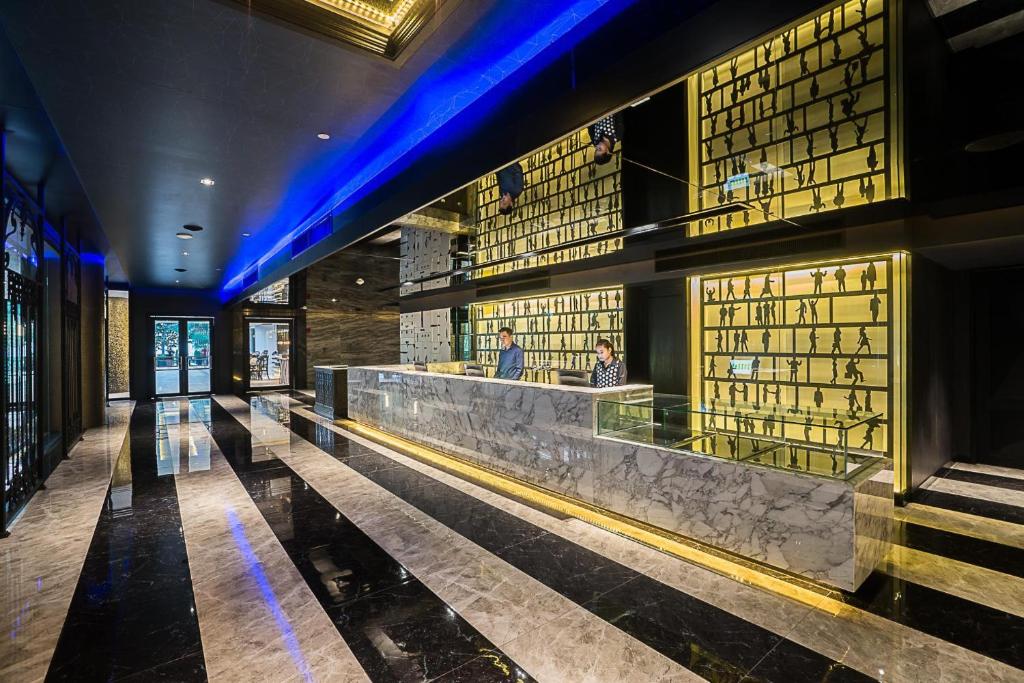 Mūsdienīgs viesnīcas reģistratūras interjers ar melnu un baltu grīdu, apgaismojumu un dekoratīviem elementiem. Apskatāmi darbinieki pie reģistratūras letes.