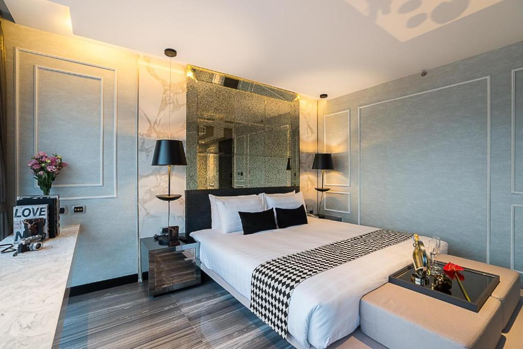 Mūsdienīgs guļamistabas interjers ar elegantiem akcentiem, tostarp melnu un baltu gultas pārklāju, stilīgu lampu un ziedu kompozīciju. Telpa ir gaiša un gaumīga, ar spoguļotu sienu un mūsdienīgu dizainu.