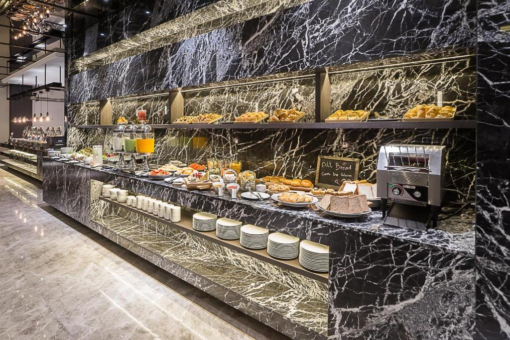 Grezna brokastu bufete ar dažādiem ēdieniem un dzērieniem, kas sakārtoti uz melna marmora galda. Iekārtojums ir moderns un stilīgs, radot elegantu atmosfēru.