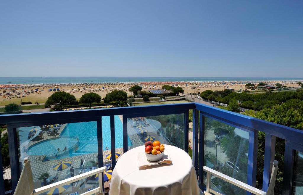 Skats no balkona uz pludmali ar sauļošanās krēsliem un peldbaseinu. Uz galda ir augļu trauks, kas piešķir telpai patīkamu atmosfēru.