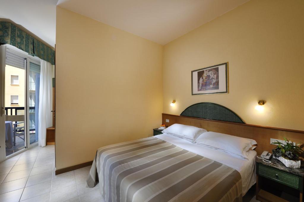 Mūsdienīgs viesnīcas numurs ar divguļamo gultu, gaišām sienām un balkonu, kas sniedz dabu. Numurā ir arī neliela atpūtas zona un mākslas darbs pie sienas.