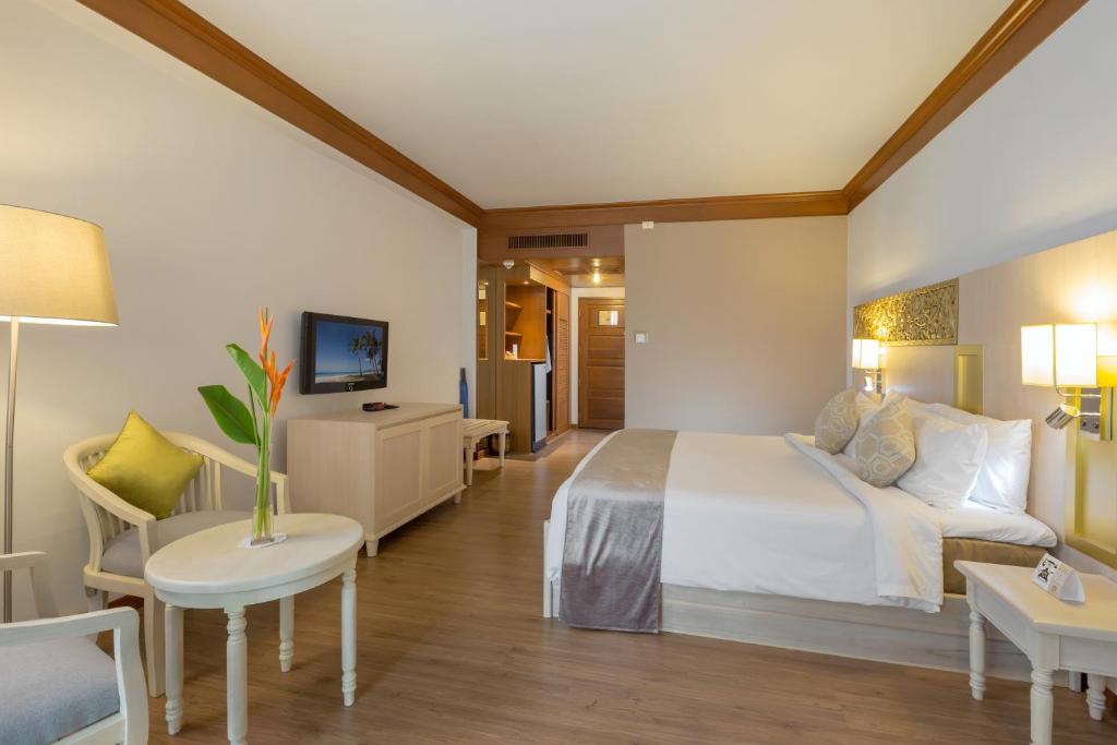 Mūsdienīgs viesnīcas numurs ar gultu, viesistabu un televizoru, kas veidots ar siltām krāsām un elegantu dizainu. Numurā ir arī gaismas avots un dekoratīva auga kompozīcija.