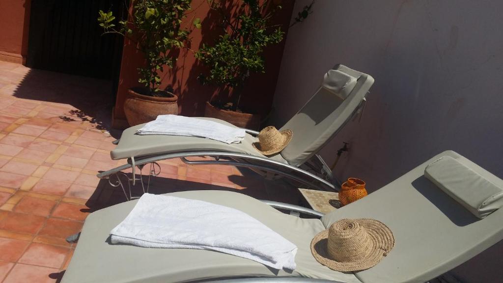 Atpūtas zona ar divām saules gultām, uz kurām novietotas baltas dvieļi un salmu cepures. Apkārt ir augi un terases flīzes, radot relaksējošu atmosfēru.