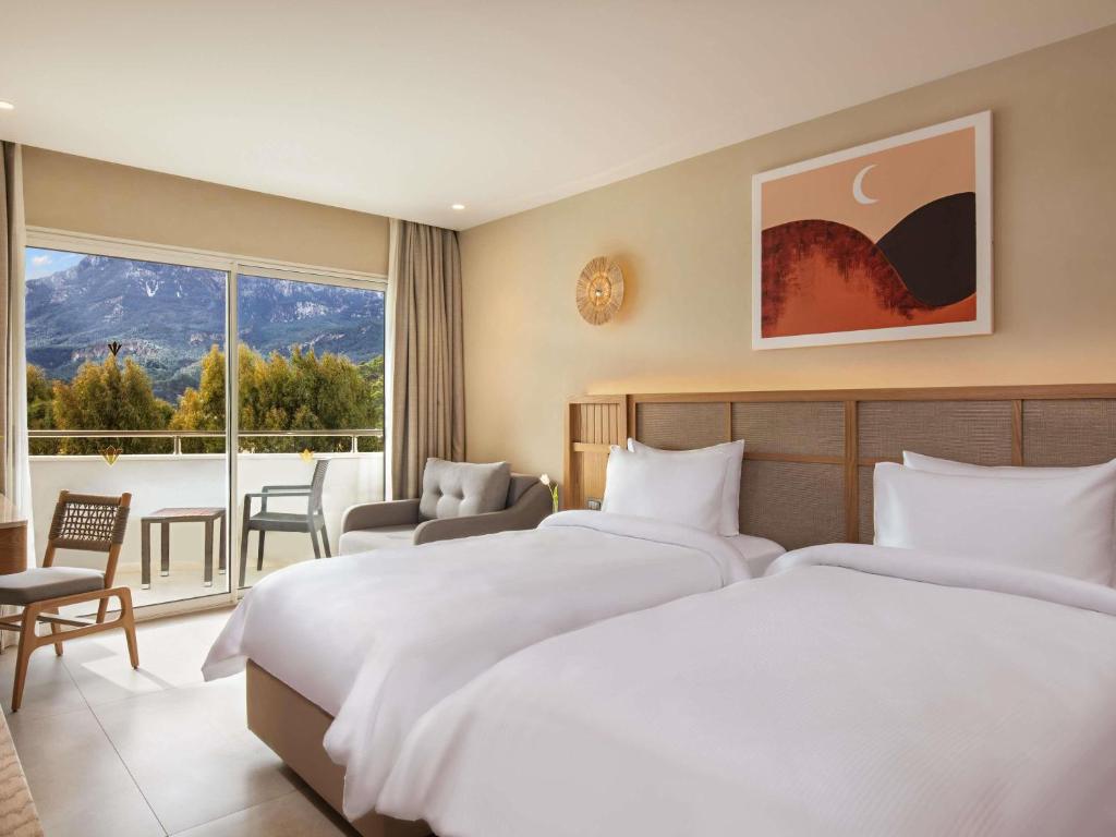 Numurs ar divām gultām un skatu uz kalniem viesnīcā Rixos Premium Tekirova.