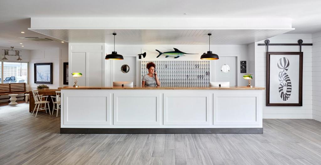 Reģistratūra ar modernu dizainu un gaismas elementiem, kur strādā darbiniece. Interjerā redzami mākslas darbi un jūras motīvi.