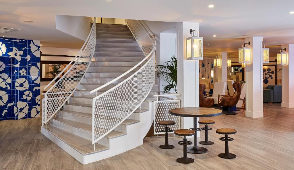 Mūsdienīgs interjers ar elegantu kāpņu dizainu un zilu flīžu sienu, kas rotāta ar ziedu motīviem. Telpā ir arī gaiši apgaismojuma elementi un ērti sēdvietas.