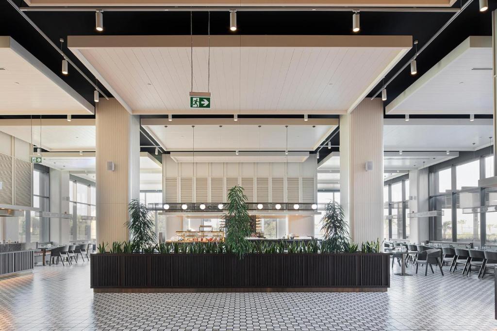 Mūsdienīgs restorāns Voyage Belek Golf & Spa ar plašām logiem un zaļumiem.