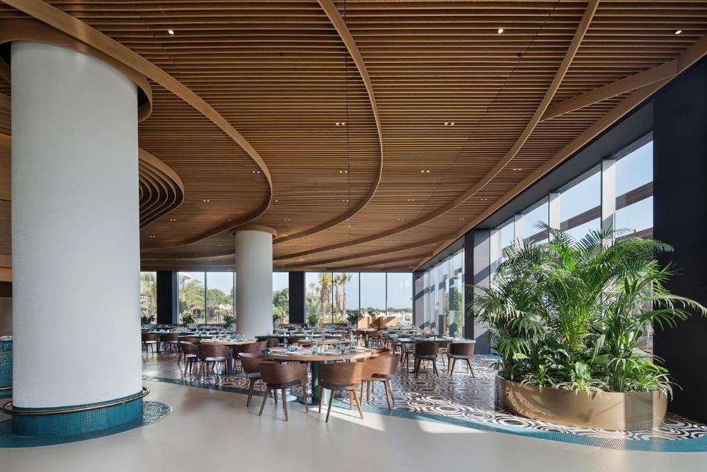 Mūsdienīgs restorāns ar lieliem logiem un elegantiem galdiem, Voyage Belek Golf & Spa.