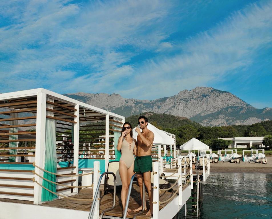 Pāris, kas bauda atpūtu pie Sherwood Exclusive Kemer pludmales, ar kalniem fona.