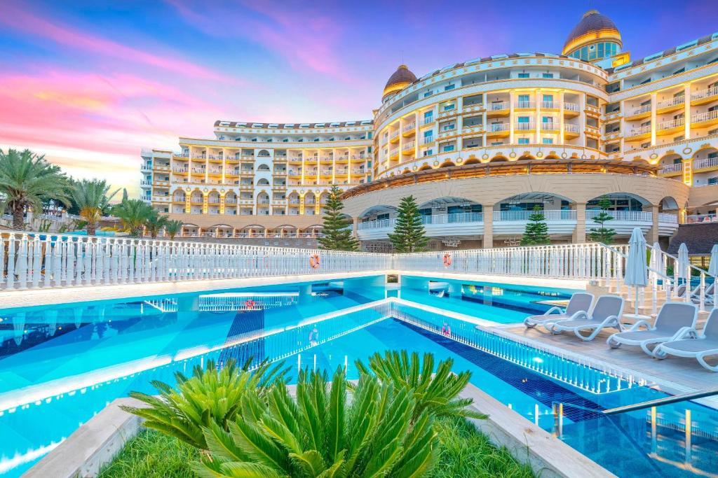 Viesnīca Kirman Sidemarin Beach & Spa ar baseinu un tropiskām ainavām pie saulrieta.
