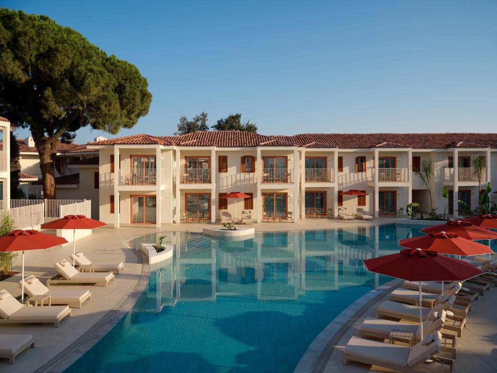Paloma Grida baseins ar sauļošanās krēsliem un sarkanām saulessargiem.