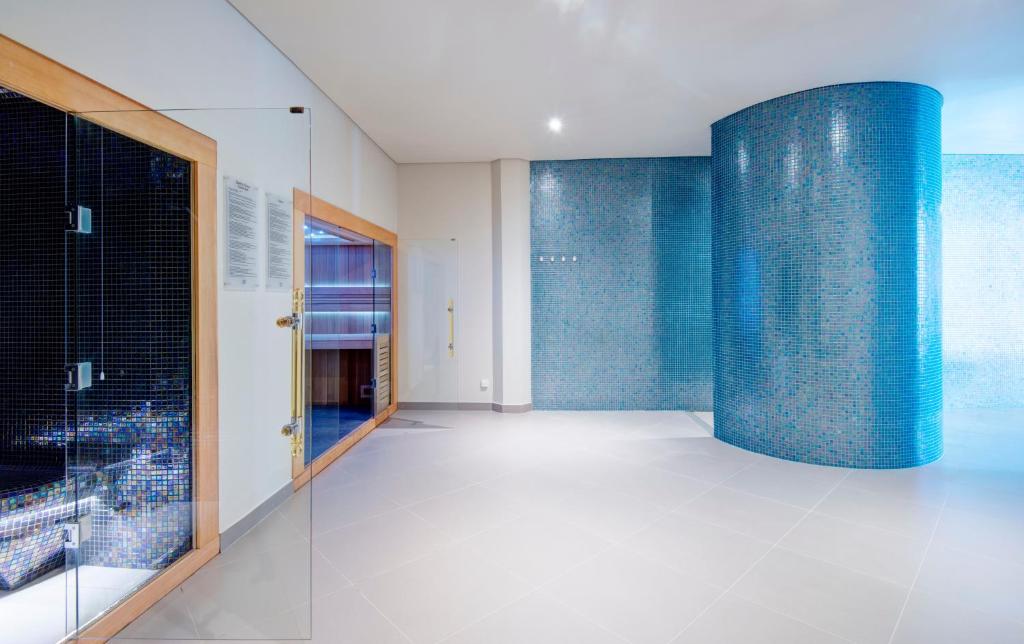 Mūsdienīga spa telpa ar zilām mozaīkas flīzēm, caurspīdīgām durvīm un relaksācijas zonām. Telpas dizains veicina mierīgu un atbrīvojošu atmosfēru.