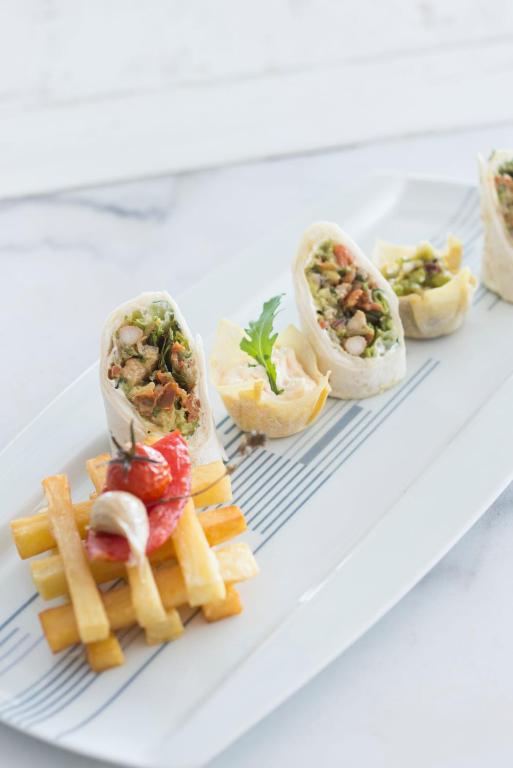 Svaigi pagatavots sushi rullis ar dārzeņiem un riekstiem, pasniegts uz eleganta šķīvja kopā ar ceptām kartupeļu nūjiņām un dekoratīviem tomātiem.