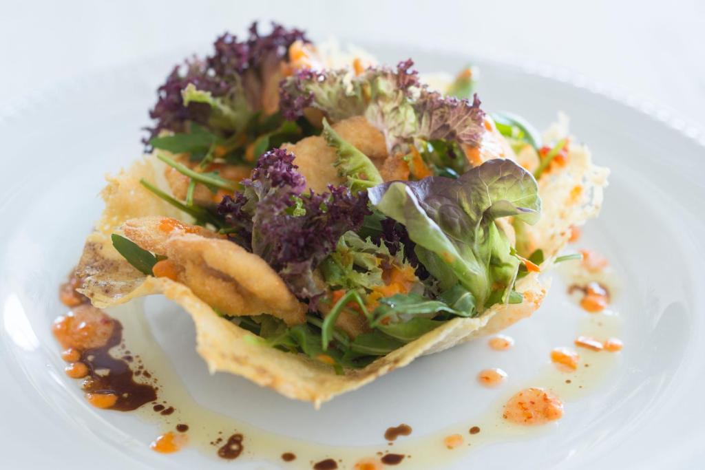 Svaiga salātu porcija kraukšķīgā čipsu traukā, dekorēta ar dažādām zaļām lapām un mērci.