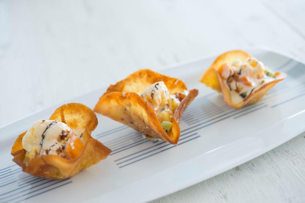 Kārdinošu uzkodu trīs porcijas uz balta šķīvja, katra no tām pildīta ar krēmīgu pildījumu un dekorēta ar dārzeņiem.