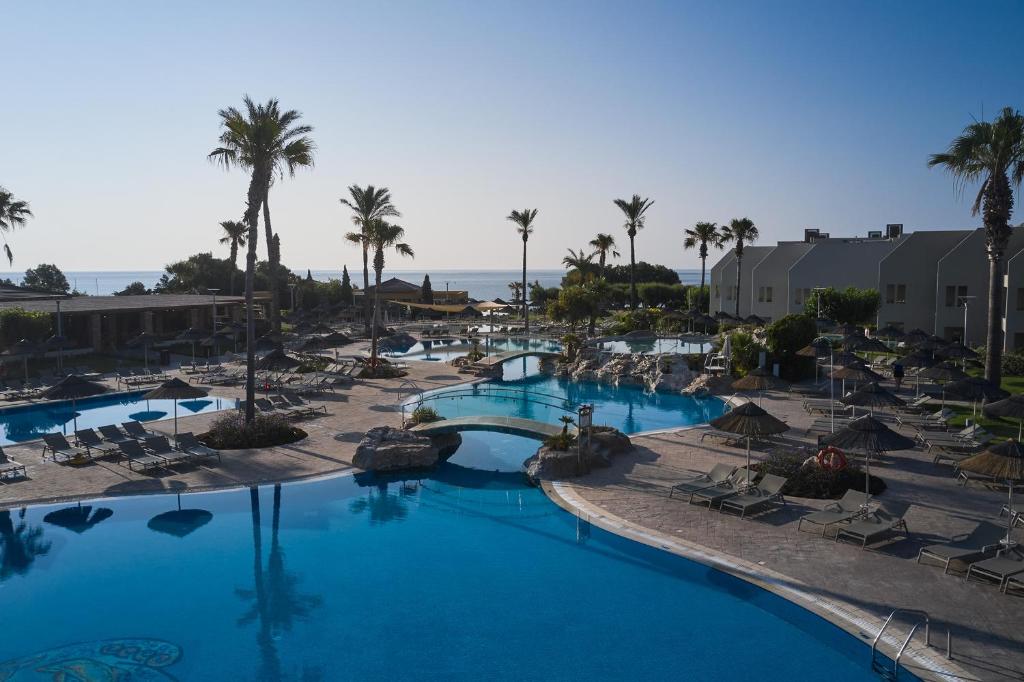 Atlantica Aegean Blue viesnīcas baseins piekrastē ar palmām.