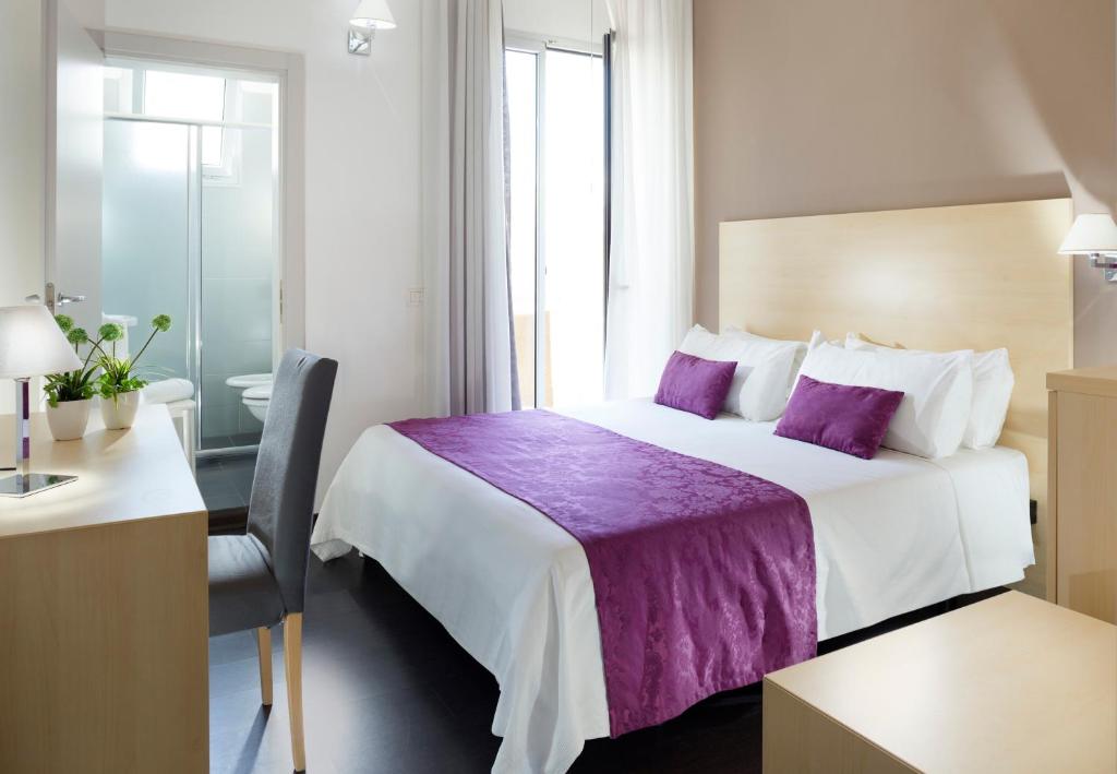 Mūsdienīga viesnīcas numuriņa iekārtojums ar divguļamo gultu, purpura krāsas gultas pārklāju un spilveniem, kā arī rakstāmgaldu un augu dekoru. Logi nodrošina dabīgu apgaismojumu un piekļuvi vannas istabai.