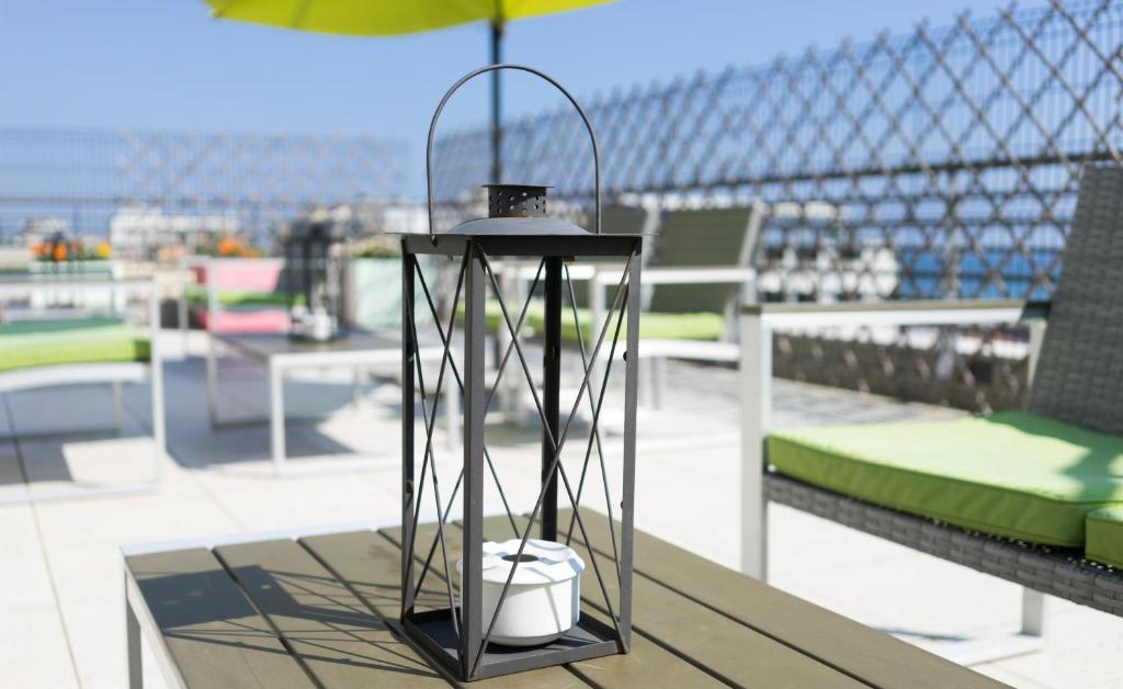 Dekoratīva laterna uz terases galda, ar zaļām mēbelēm un skatu uz jūru. Ideāla atmosfēras radīšanai ārpus telpām.