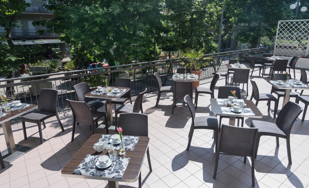 Āra terase ar galds un krēsliem, rotāta ar ziediem un galda piederumiem, piedāvā patīkamu atmosfēru ēšanai brīvā dabā. Zaļi koki un saulaina gaisma papildina ainavu.