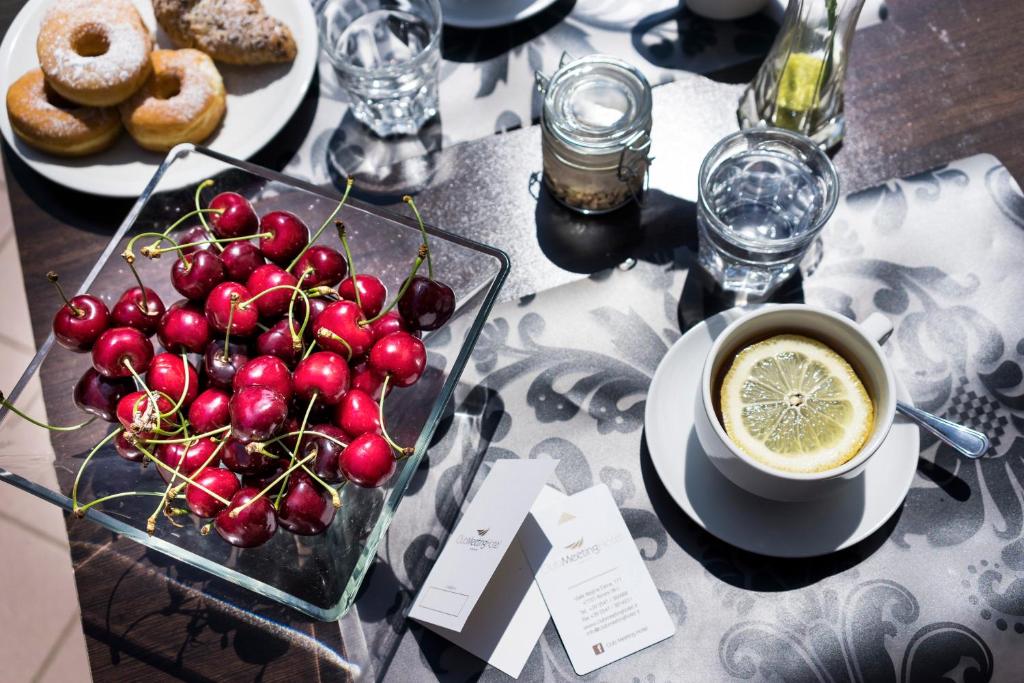 Svaigu ķiršu bļoda, tase ar citronu un dienas našķi, kas ietver donuts un konditorejas izstrādājumus, uz galda ar dekoratīvu galdautu.